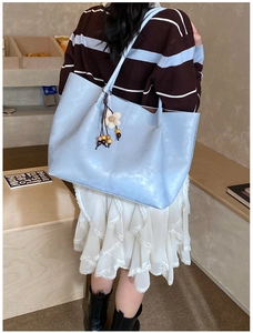 Détail du grand sac cabas bleu clair avec breloque fleurie porté à l'épaule du modèle