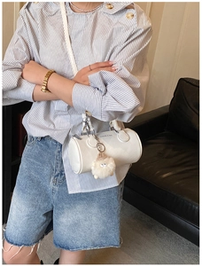 Close-up of white PU leather cylinder bag with lamb pendant and fashion text detail