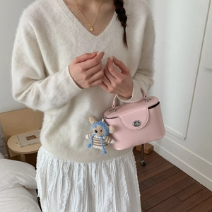 Detail of pink box bag with silver twist lock and cute knitted bear charm on a white outfit