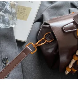 Close-up of vintage brown leather handbag with antique gold hooks and wooden bead tassel