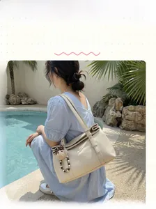 Detailed view of a cream leather tote bag with a cute plush bear pendant on the strap