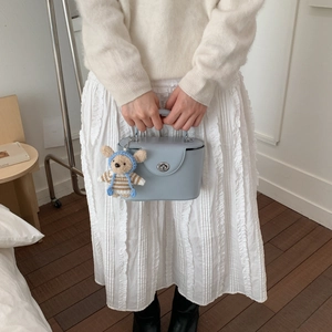 Close-up of a light blue bucket bag with a plush bear charm and silver twist lock