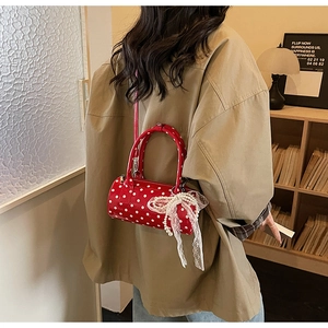 Red polka dot cylindrical handbag with pearl lace bow detail worn by a model