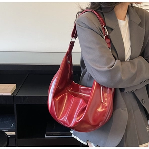 Deep red patent leather crescent bag worn by a model in an elegant indoor setting