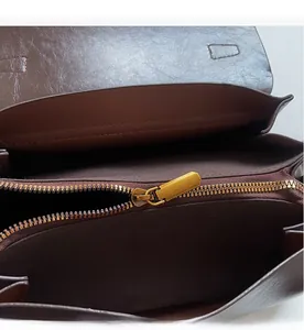 Close-up of smooth gold metal zipper and stitching on a dark brown leather handbag