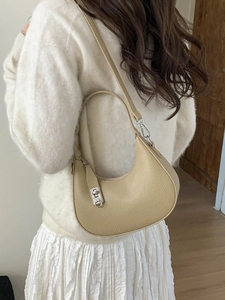 Chic beige dumpling handbag with litchi grain and silver buckle, worn as a shoulder bag