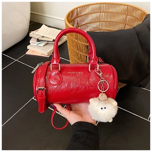 Close-up of red glossy pleated Boston bag with silver hardware and plush lamb charm