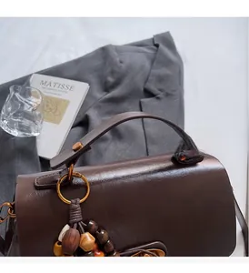 Detail of dark brown leather handbag with wooden bead charm and golden ring on grey blazer