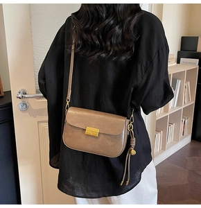 Detail of tan leather crossbody bag featuring gold buckle and fringe charm with model