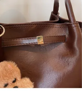Detail of dark brown leather tote bag with gold metal buckle and decorative plush bear