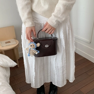 Close-up of a dark brown leather box bag featuring a silver twist lock and teddy bear charm