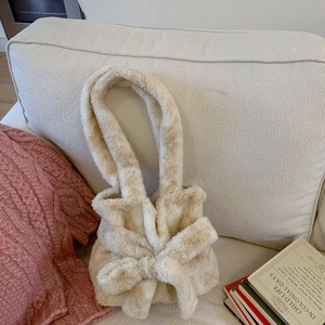 Close-up of cream fuzzy handbag with large plush bow and soft lamb wool texture