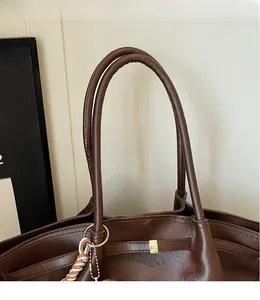 Detail of deep brown leather tote bag with gold lock and braided lanyard accessory