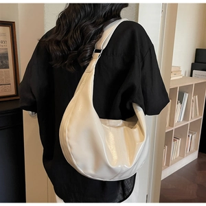 Rear view of model wearing a large creamy white crescent bag in glossy patent leather