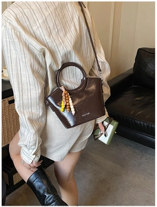Detail of a brown glossy leather bucket bag featuring colorful wooden bead charms