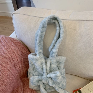 Close-up of light blue plush handbag with a cute bow detail on a soft sofa