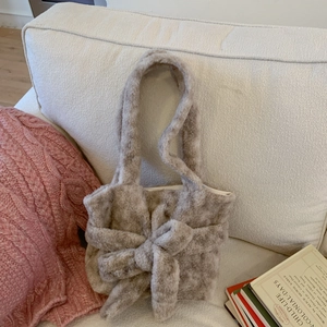 Detail view of plush beige shoulder bag with oversized bow and soft faux fur texture
