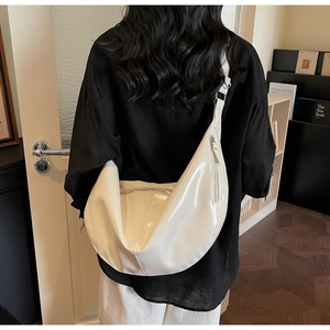 Detail of white glossy crescent bag with silver metallic zippers and wide strap on model
