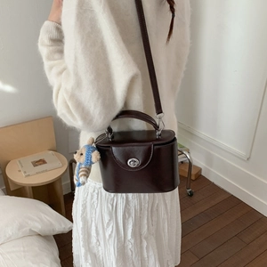 Detail of dark brown leather box bag with silver twist lock and cute teddy bear charm