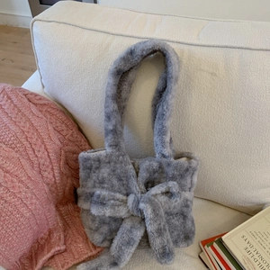 Detail of grey plush tote bag featuring a large bow and soft faux fur texture