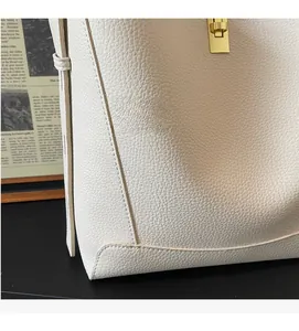 Detailansicht aus weißem Leder mit Kieselmaserung und goldenem Metallschloss am Shopper