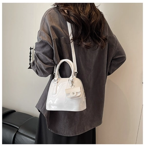 Detail of a white glossy shell-shaped handbag with a mini decorative charm pouch