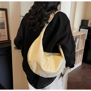 Détail d'un sac hobo en cuir verni beige brillant porté à l'épaule pour femme