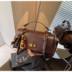 Detail of dark brown vintage handbag with oval metal lock and wooden bead tassel decor