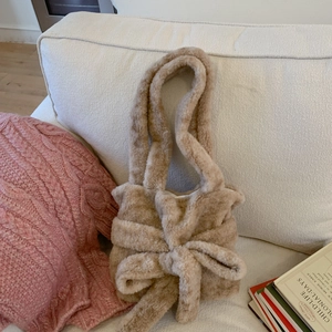 Brown plush handbag with large bow detail displayed on white fabric and vintage books
