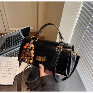 Close-up of black handbag with golden twist lock and decorative wooden bead tassel