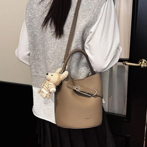 Detail der khakifarbenen Beuteltasche aus Leder mit Plüschbär-Anhänger und Metallschnalle
