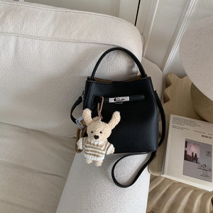 Detail of black lychee grain bucket bag with silver buckle and cute teddy bear charm