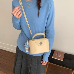 Detail of beige box bag with silver twist lock and cute plush bear charm on blue hoodie