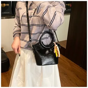 Detail of glossy black patent leather bucket bag with colorful ethnic beaded pendant