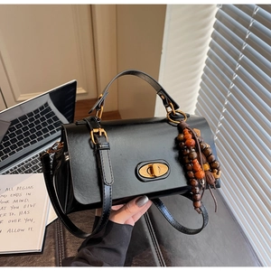 Close-up of black glossy crossbody bag with golden twist lock and decorative wood beads