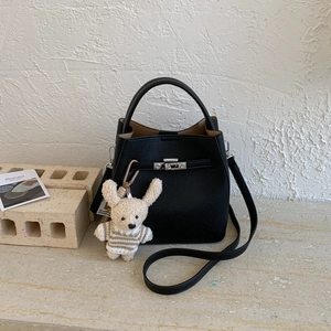 Detail of black lychee grain leather bucket bag with silver lock and plush toy charm