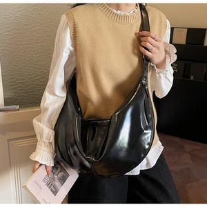 Detail of a large black glossy crescent crossbody bag shown on a model in a casual setting