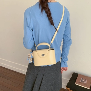 Detail of light yellow structured crossbody bag with a cute bear charm and silver twist lock