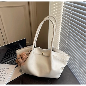 Detail of minimalist cream tote bag with gold buckle and brown plush bear charm