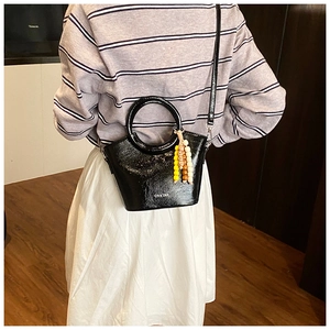Detail view of a black glossy bucket bag with beaded tassel and circular handle