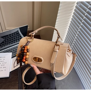 Macro detail of beige crossbody bag with metal twist lock and wooden bead tassel