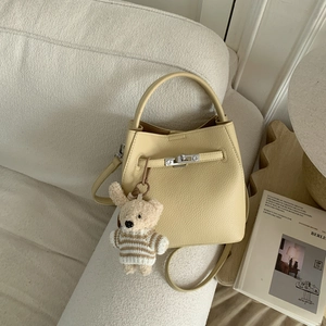 Detail of cream leather bucket bag with litchi texture and cute teddy bear charm