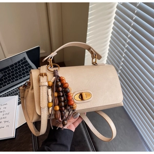 Close-up of beige crossbody bag featuring vintage wooden bead tassel and gold twist lock