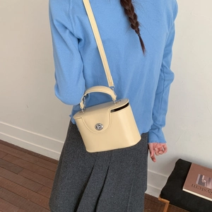 Detail of cream boxy crossbody bag featuring silver rotating lock and top handle on model