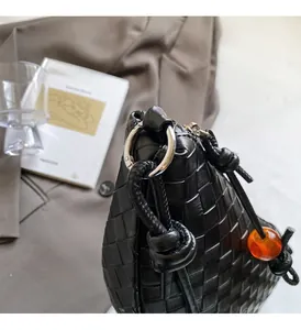 Détail du sac tressé en cuir noir avec anneau argenté et perle en résine ambrée