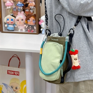 Detail of green nylon crossbody phone bag with trendy rope strap and red apple charm