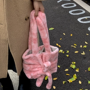 Pink plush tote bag with bow detail held by model in autumn outdoor street setting