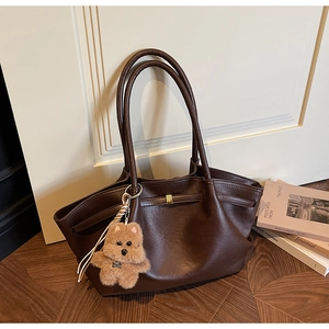 Detail of dark brown faux leather tote bag with elegant folds and a plush puppy charm