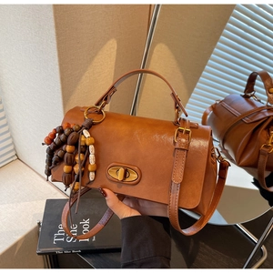 Detail view of brown vintage satchel with gold twist lock and colorful wooden beads charm