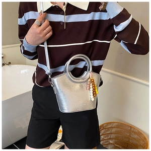 Silver metallic bucket bag with unique beaded charm shown on model in casual setting